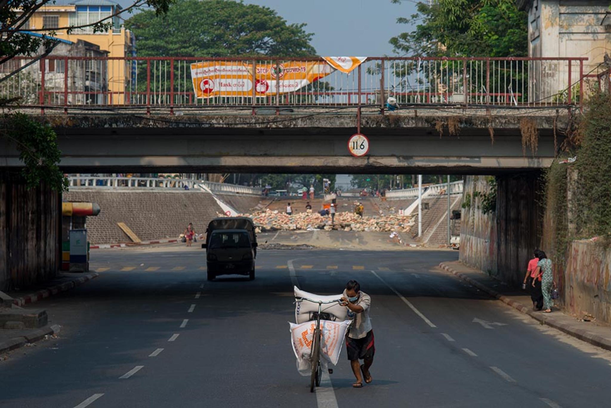 A man is pushing a bicycle, and a barricade at the intersection of Myanmar street.
