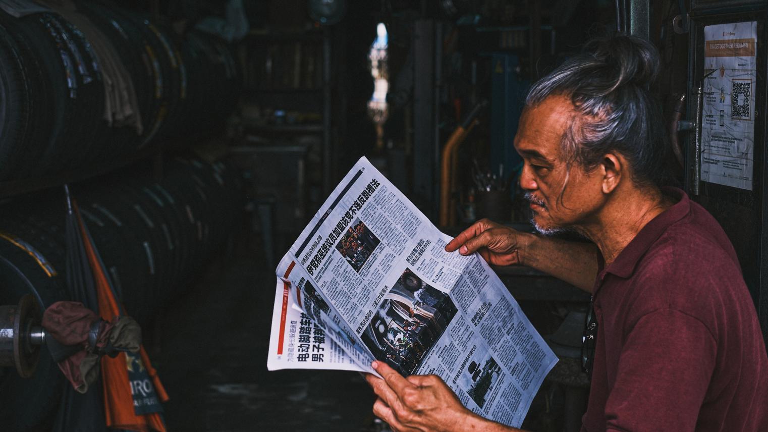 A man reads a Chinese language newspaper at a tire repair shop in Little India, Singapore.